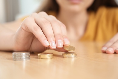 Photo of Woman stacking coins at table, focus on hand