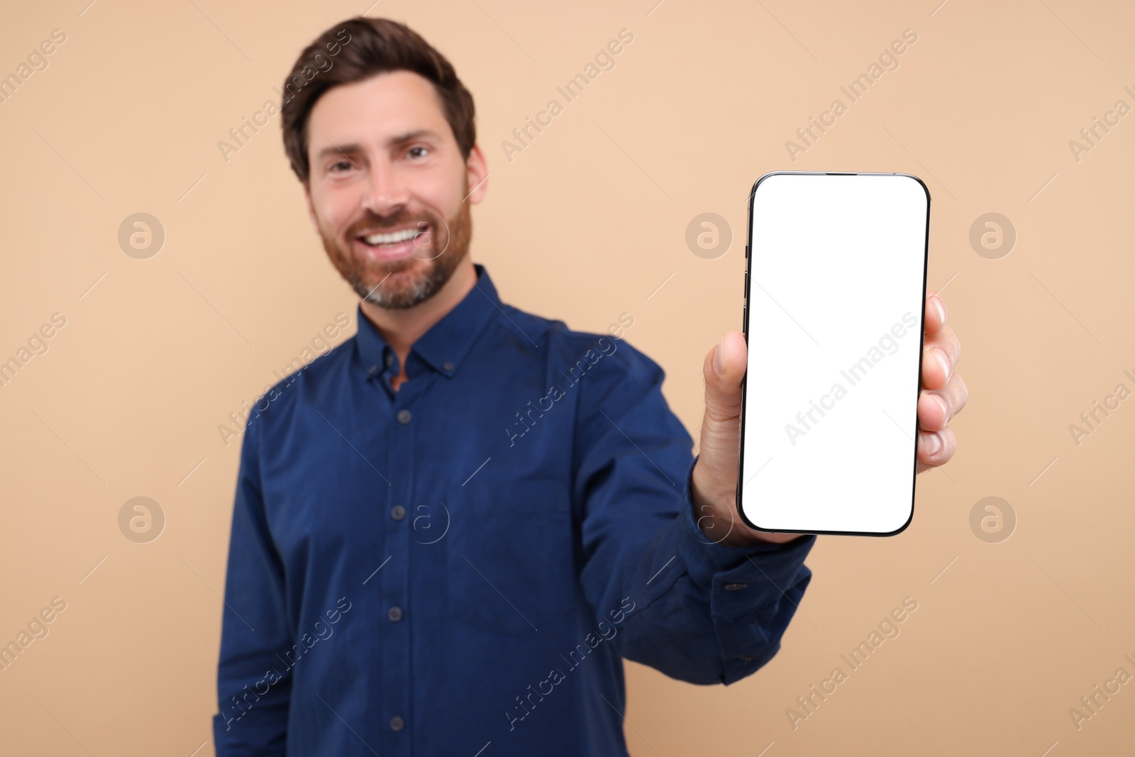 Photo of Handsome man showing smartphone in hand on light brown background, selective focus. Mockup for design