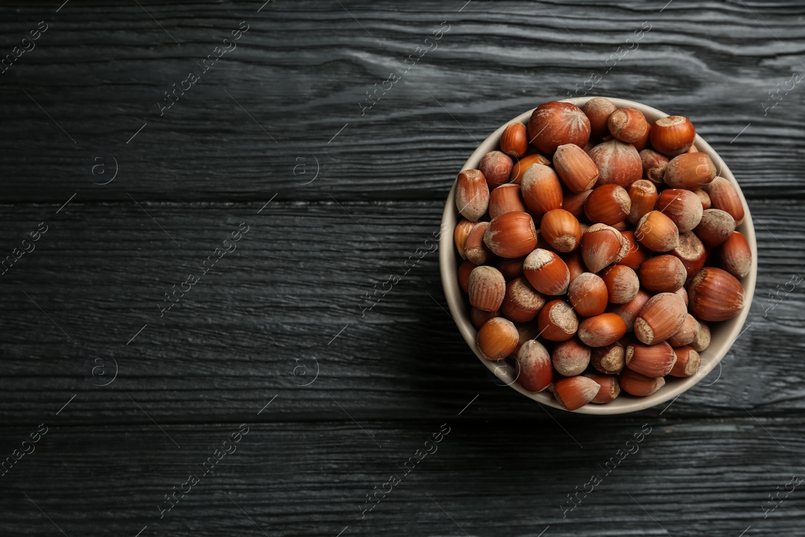 Photo of Ceramic bowl with acorns on black wooden table, top view and space for text. Cooking utensil