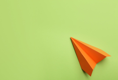 Photo of Orange paper plane on green background, top view. Space for text