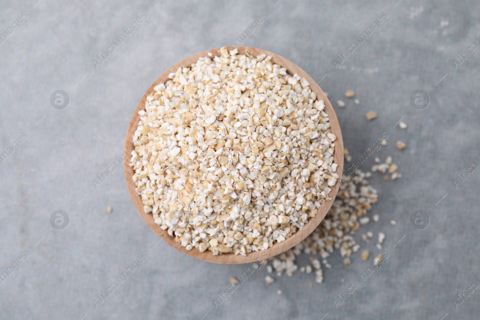 Photo of Raw barley groats in bowl on grey table, top view