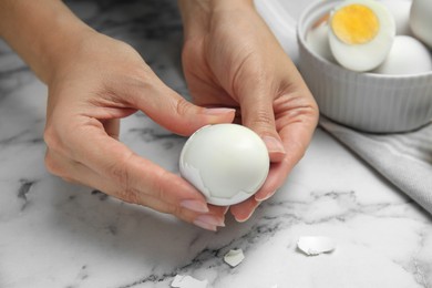 Photo of Woman peeling boiled egg at white marble table, closeup
