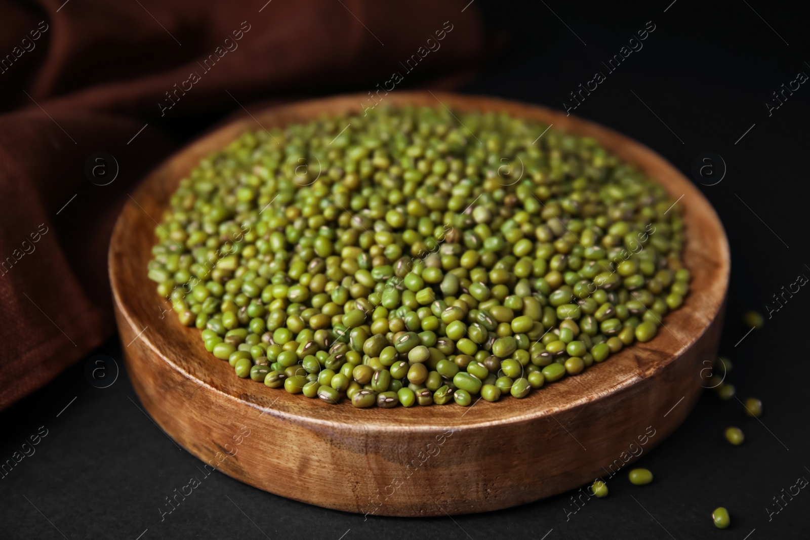 Photo of Wooden bowl with green mung beans and napkin on black background, closeup