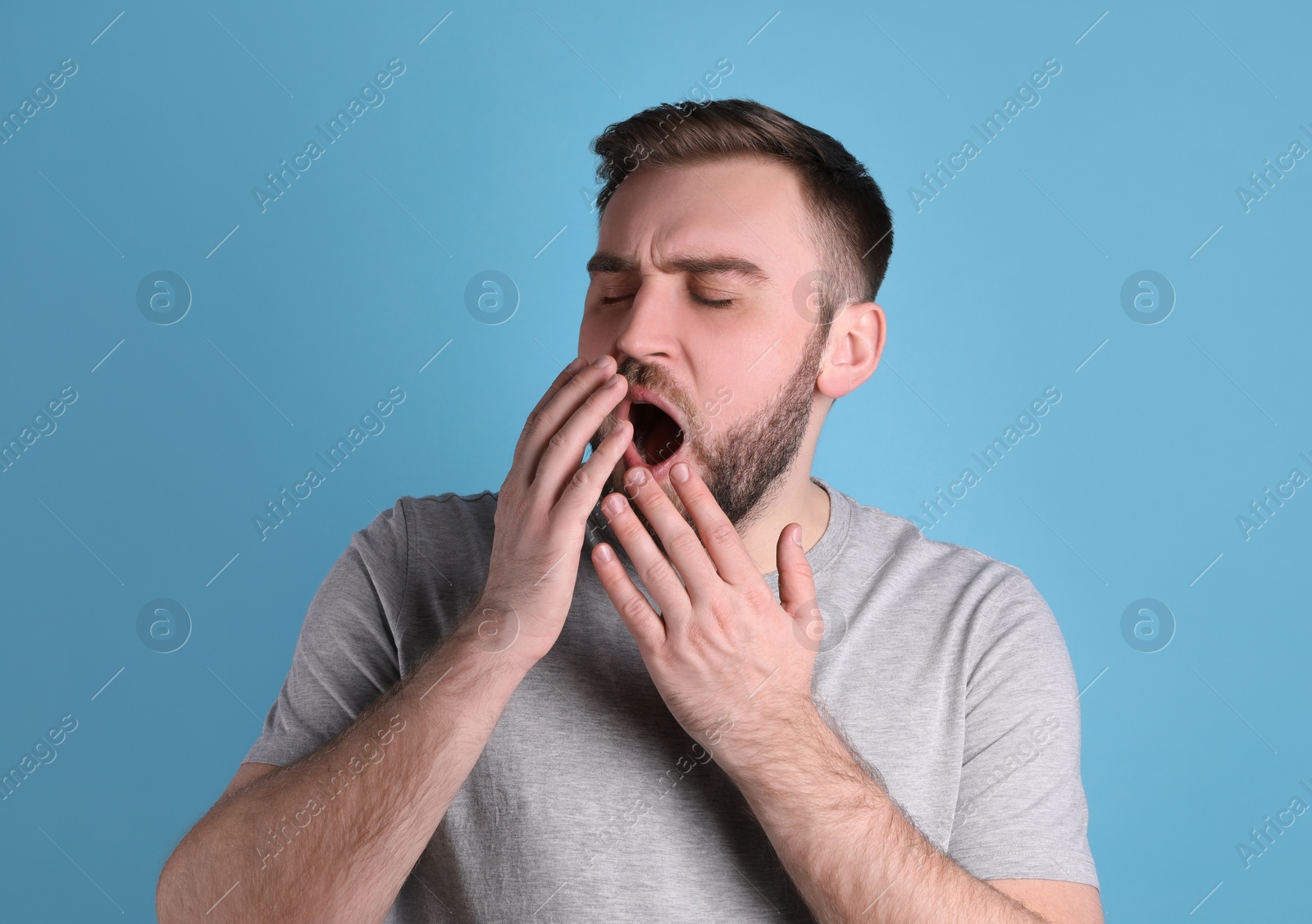 Photo of Sleepy young man yawning on light blue background