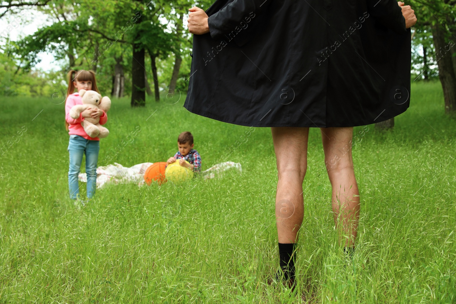 Photo of Male exhibitionist opening his coat in front of kids outdoors. Child in danger