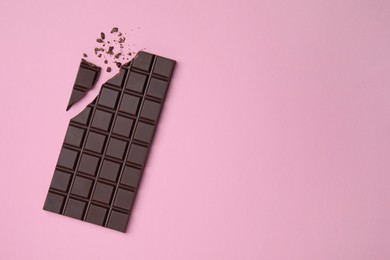 Photo of Broken dark chocolate bar on pink background, flat lay. Space for text