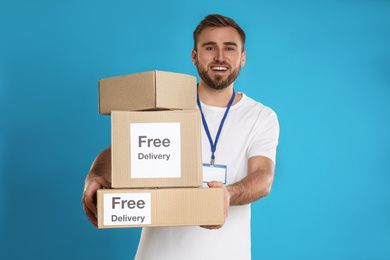 Male courier holding parcels with stickers Free Delivery on light blue background