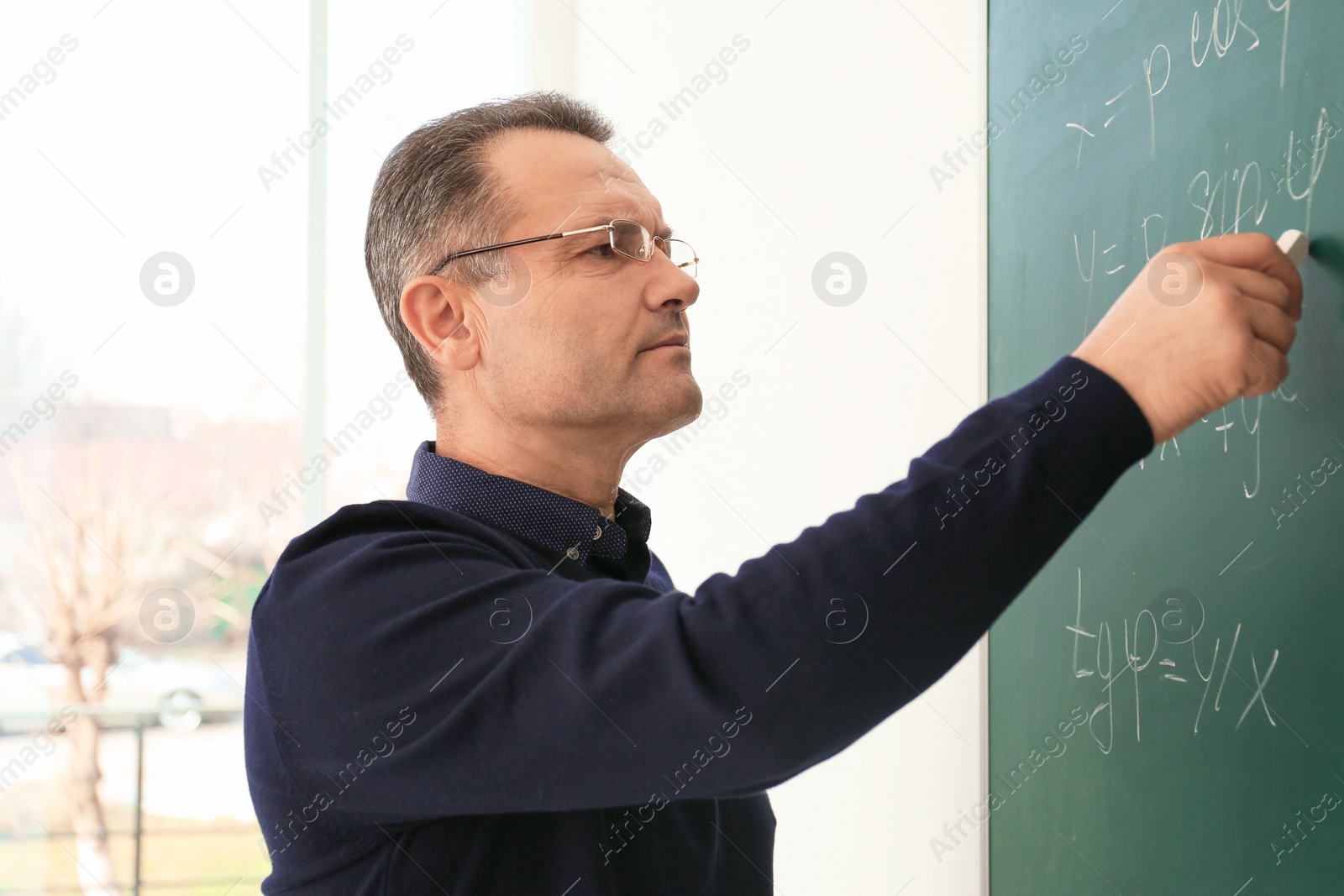 Photo of Male teacher writing on blackboard in classroom