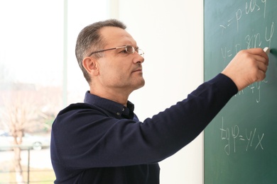 Male teacher writing on blackboard in classroom