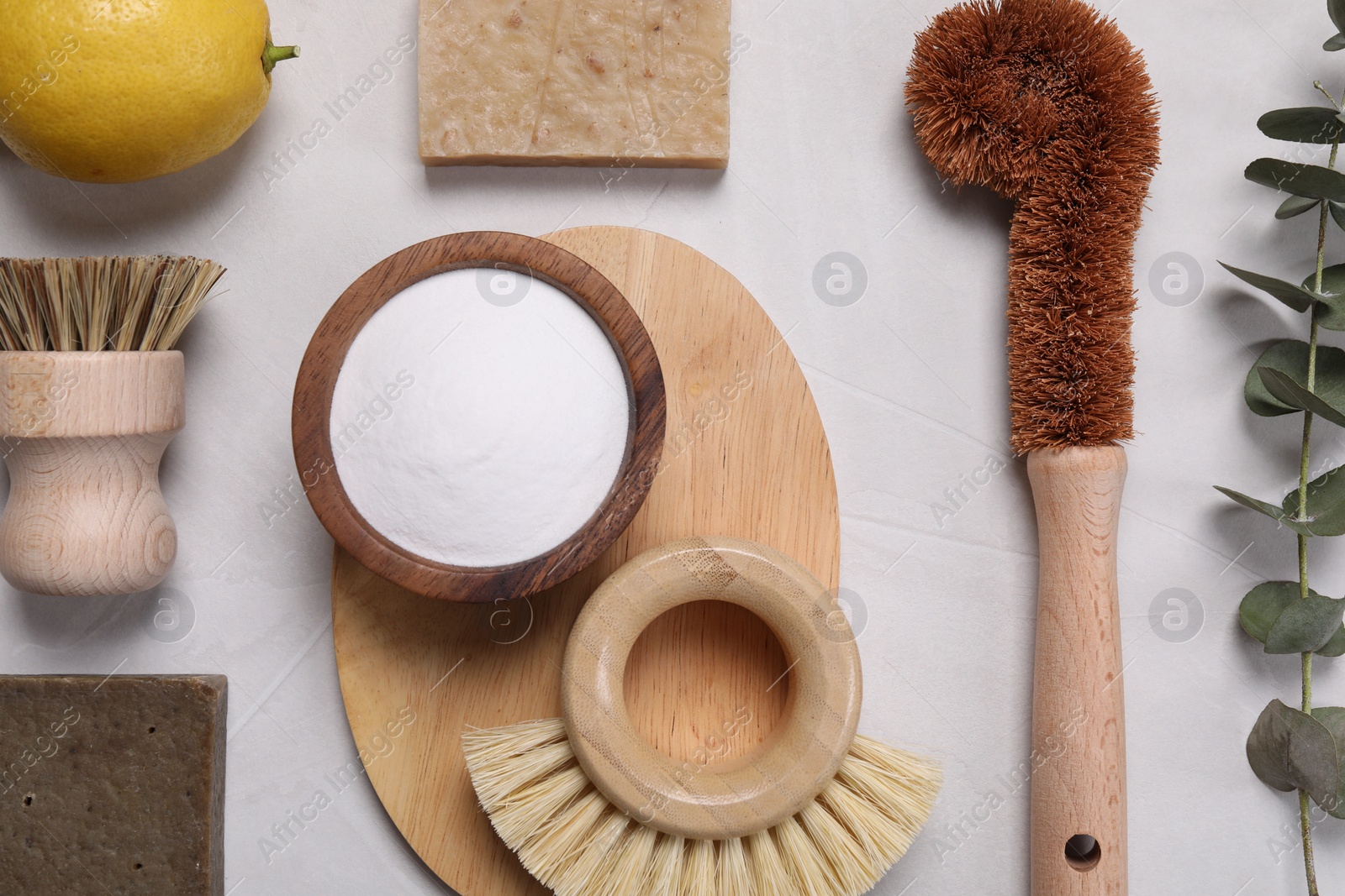 Photo of Cleaning brushes, baking soda, lemon, soap bar and eucalyptus leaves on white table, flat lay