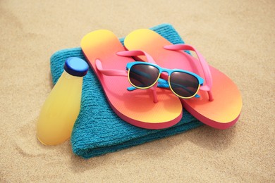 Stylish sunglasses, flip flops, towel and bottle of refreshing drink on sand