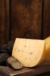 Photo of Delicious cheese and fresh black truffles on wooden board. Space for text