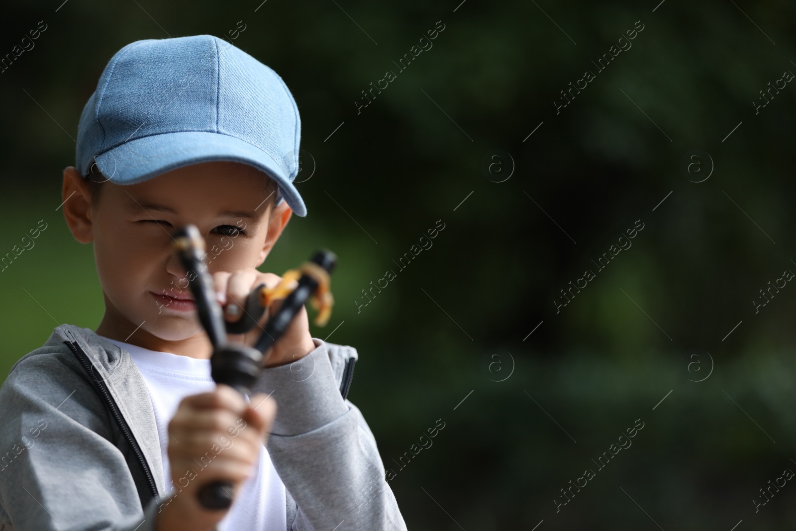 Photo of Little boy playing with slingshot outdoors. Space for text