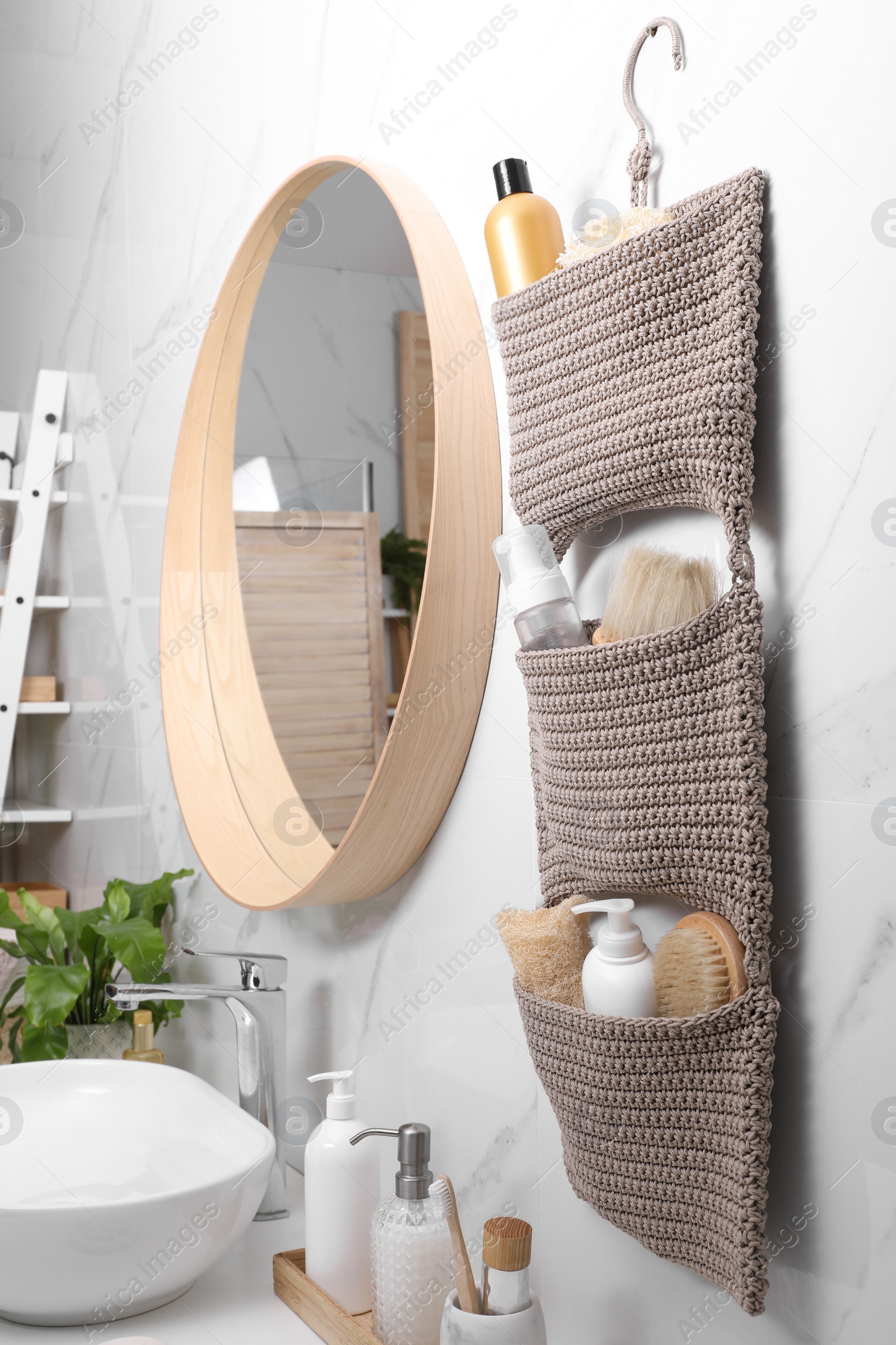 Photo of Storage with essentials hanging near mirror on white marble wall in bathroom. Stylish accessory