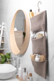 Photo of Storage with essentials hanging near mirror on white marble wall in bathroom. Stylish accessory