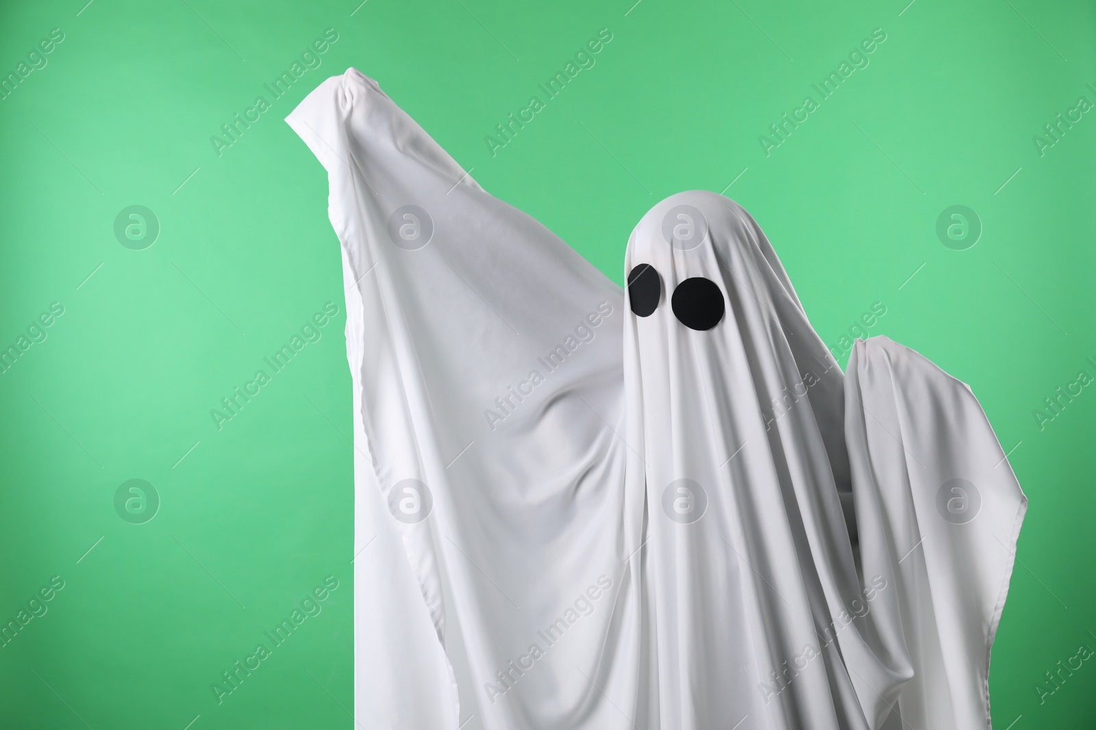 Photo of Creepy ghost. Person covered with white sheet on green background, space for text