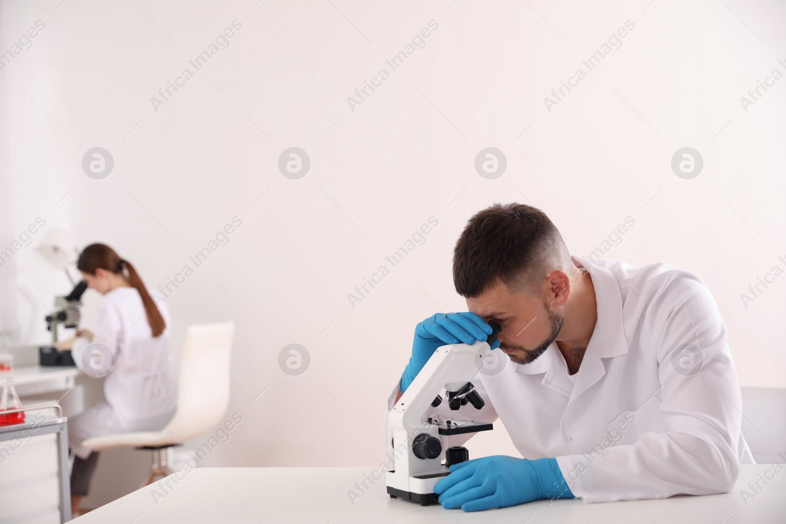 Photo of Scientist using microscope at table and colleague in laboratory. Medical research