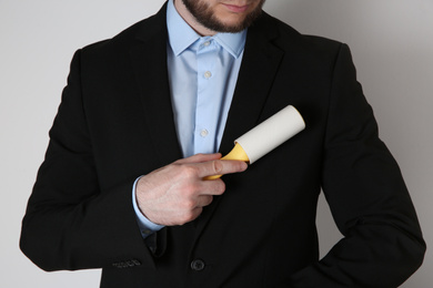 Photo of Man cleaning black jacket with lint roller on light grey background, closeup