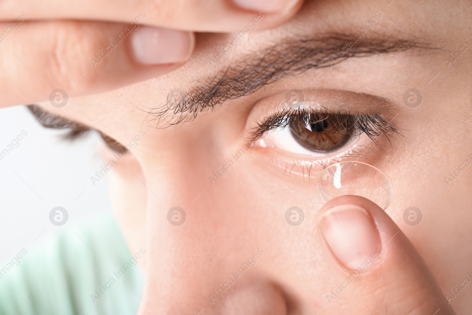 Photo of Young woman putting contact lens in her eye, closeup