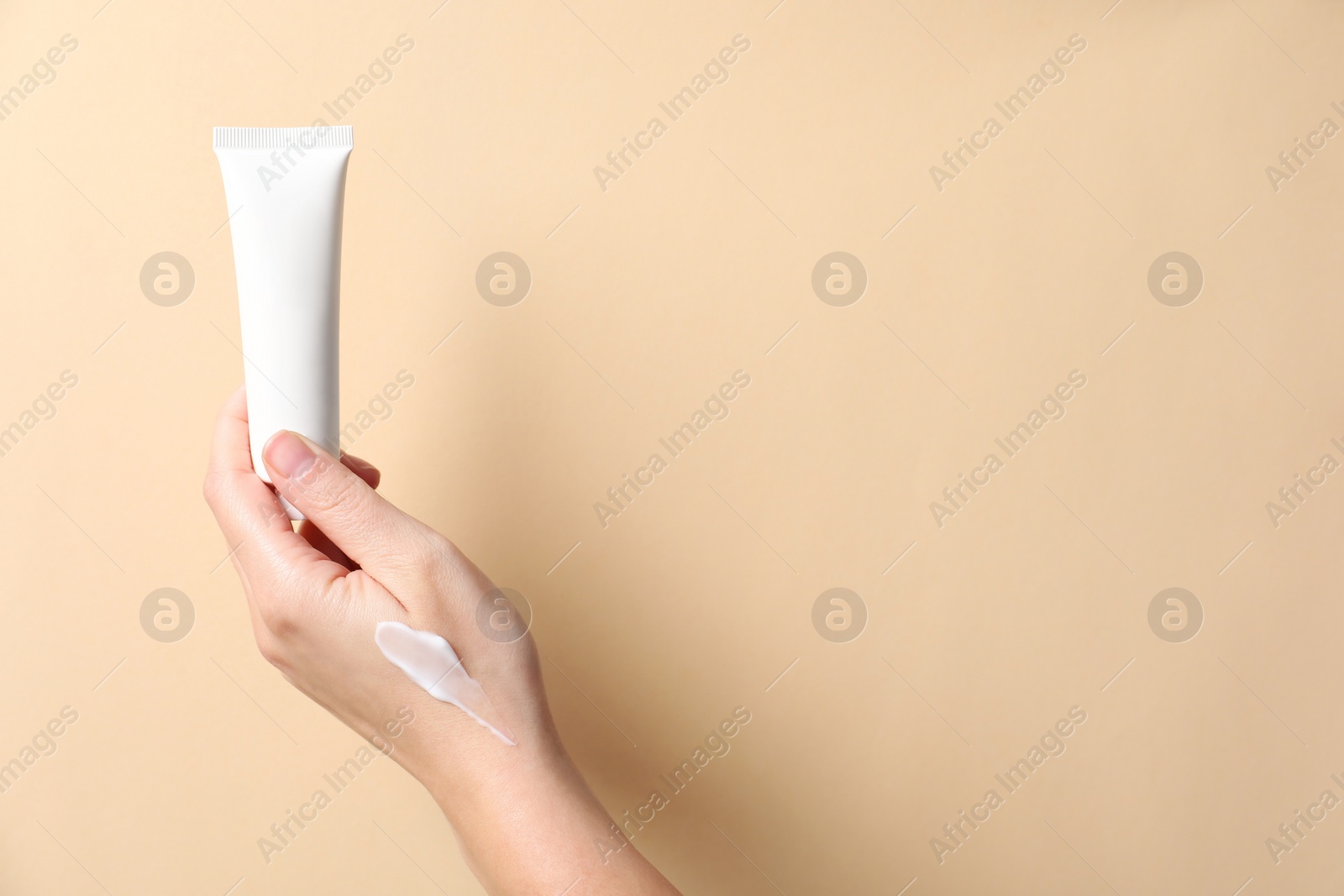 Photo of Woman with tube of hand cream on beige background, closeup. Space for text