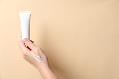 Photo of Woman with tube of hand cream on beige background, closeup. Space for text