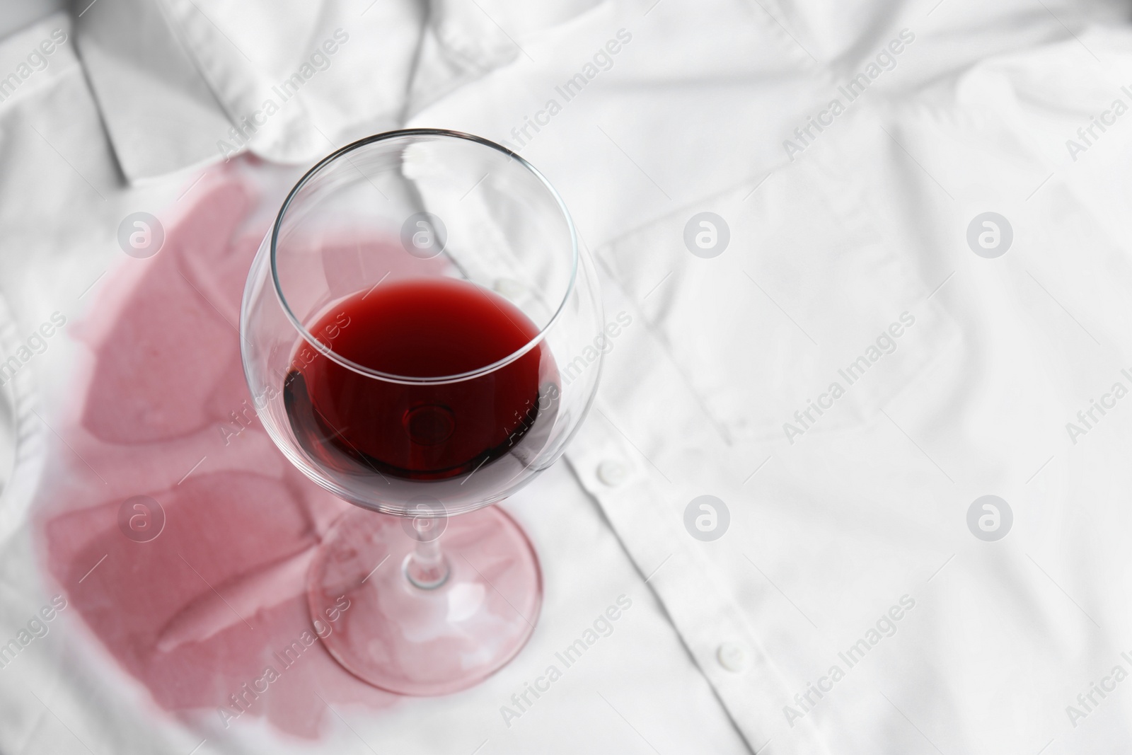 Photo of Transparent glass and spilled exquisite red wine on white shirt. Space for text