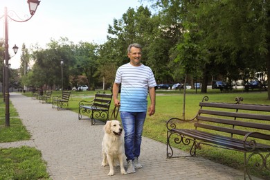 Happy senior man walking his Golden Retriever dog in park