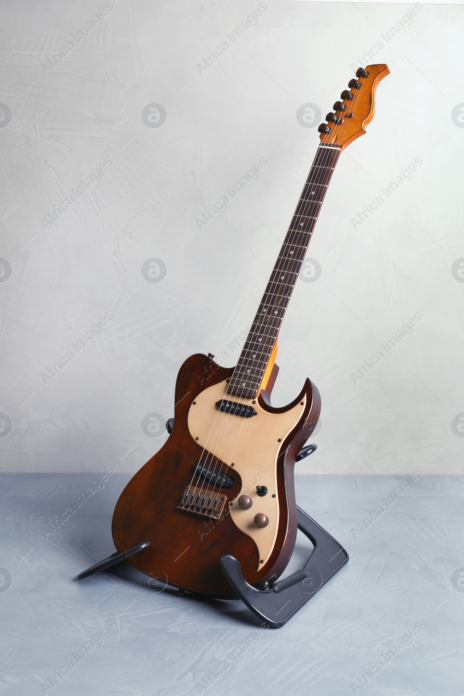 Photo of Modern electric guitar on stand near color wall