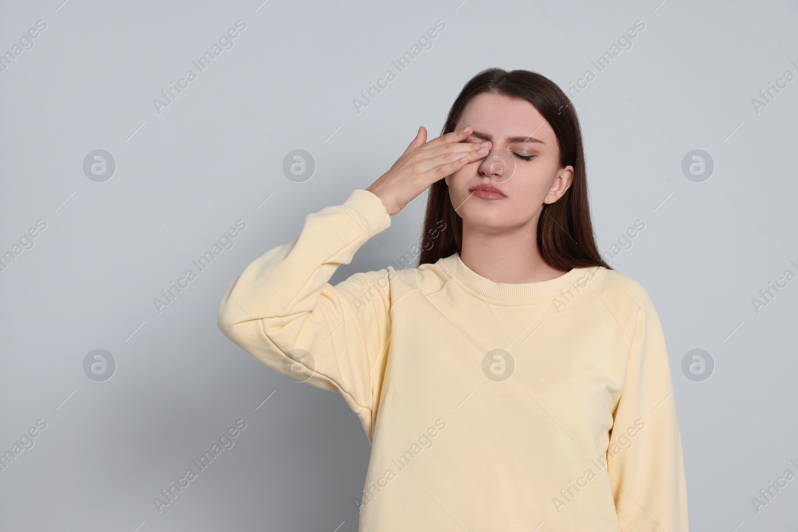 Photo of Young woman suffering from eyestrain on light background