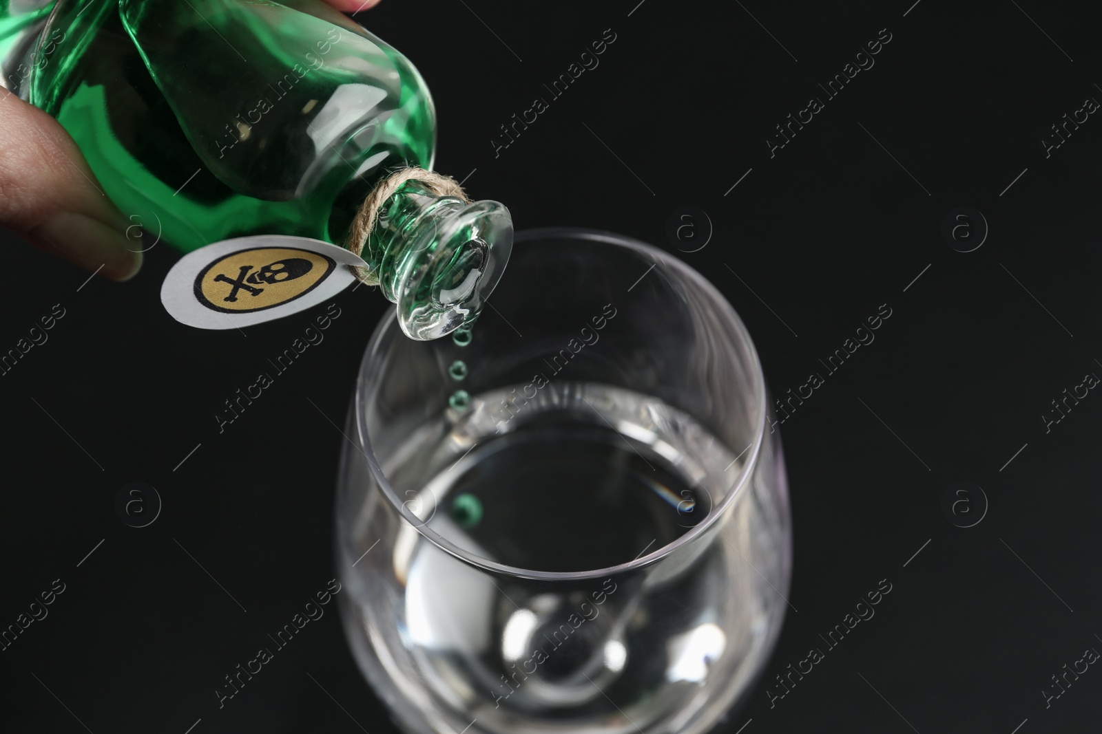 Photo of Woman pouring poison into glass of water on black background, closeup