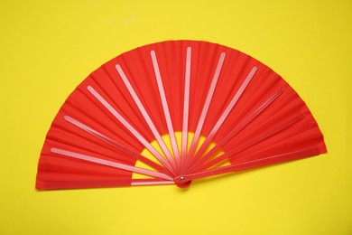 Photo of Bright red hand fan on yellow background, top view