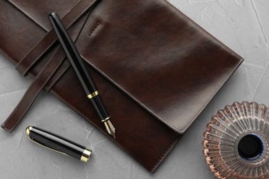 Photo of Stylish fountain pen, leather notebook and inkwell on light grey textured table, flat lay