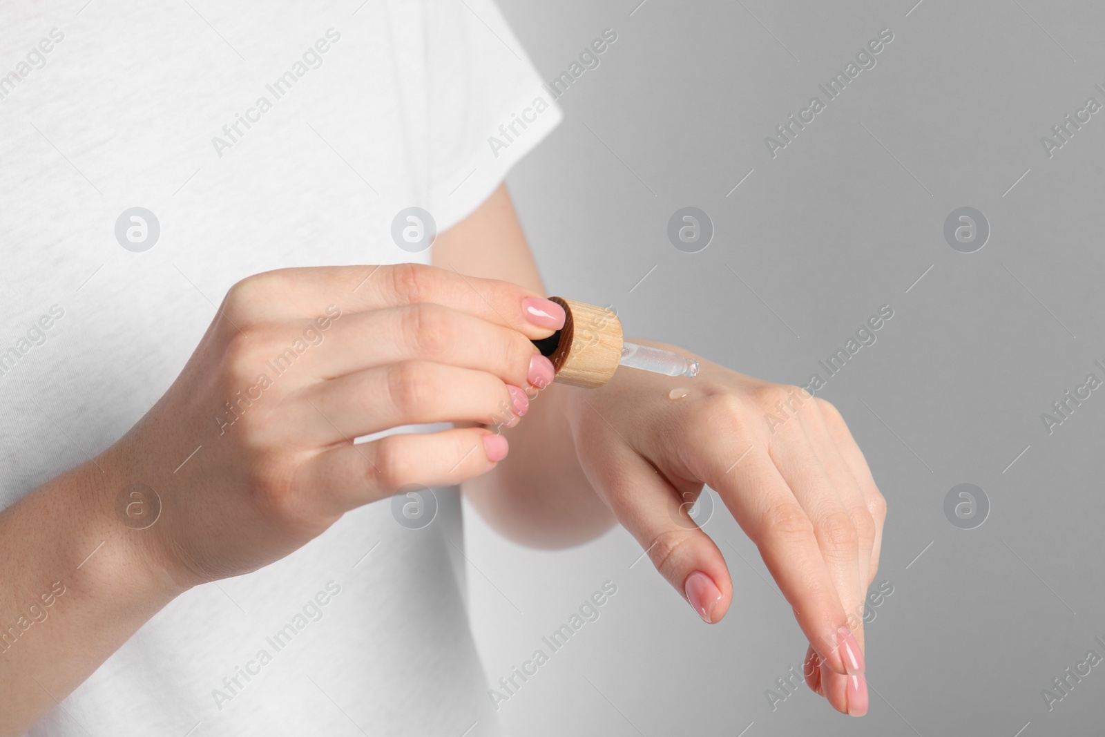 Photo of Woman dripping serum from pipette on her hand against light grey background, closeup