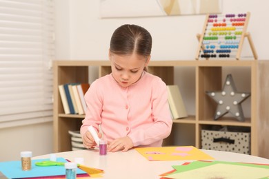 Cute little girl using glue stick at desk in room. Home workplace