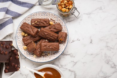 Delicious chocolate candy bars, caramel and nuts on white marble table, flat lay. Space for text