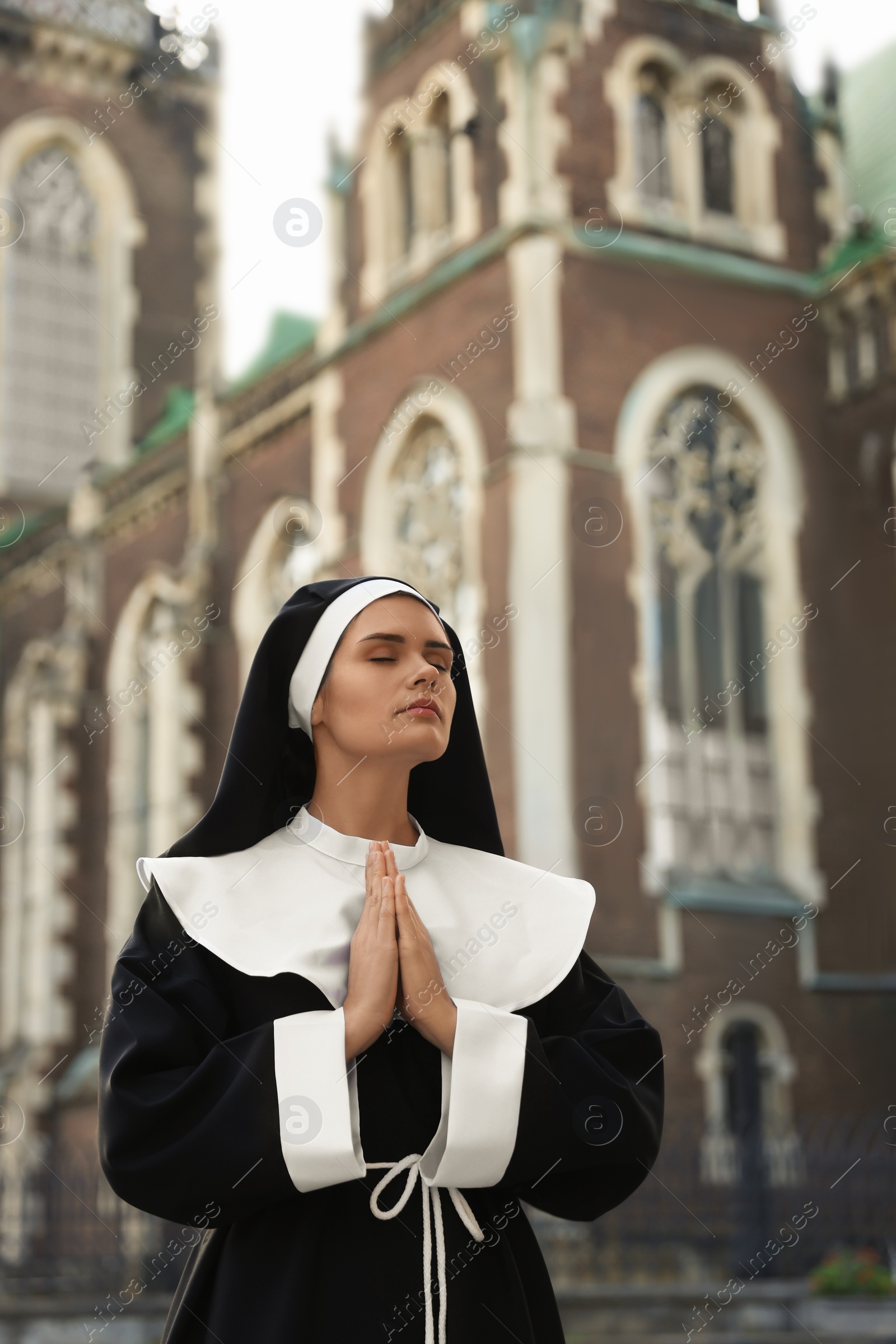 Photo of Young nun with hands clasped together while praying near cathedral outdoors