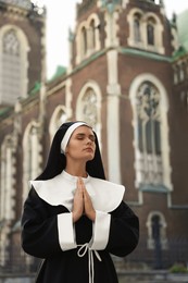 Photo of Young nun with hands clasped together while praying near cathedral outdoors