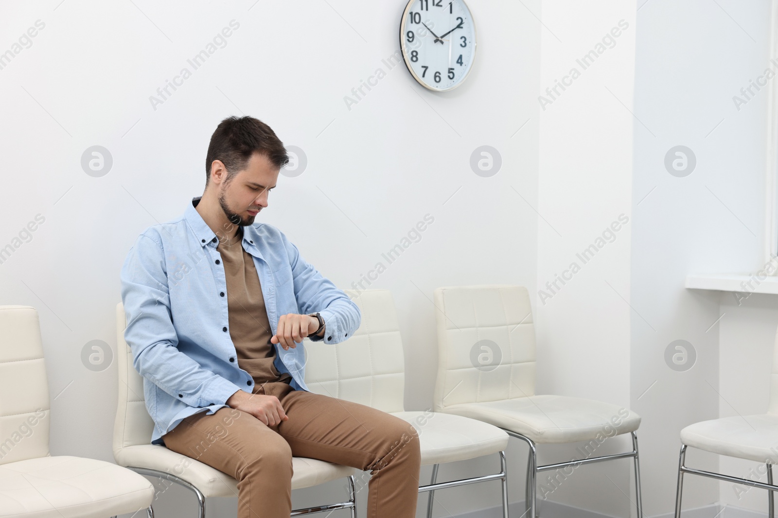 Photo of Man looking at wrist watch and waiting for appointment indoors