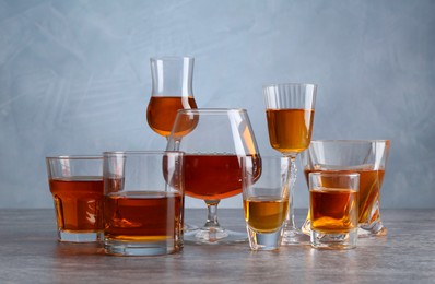 Photo of Different liqueurs in glasses on grey textured table