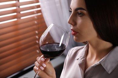 Beautiful young woman with glass of luxury red wine indoors, closeup view. Space for text