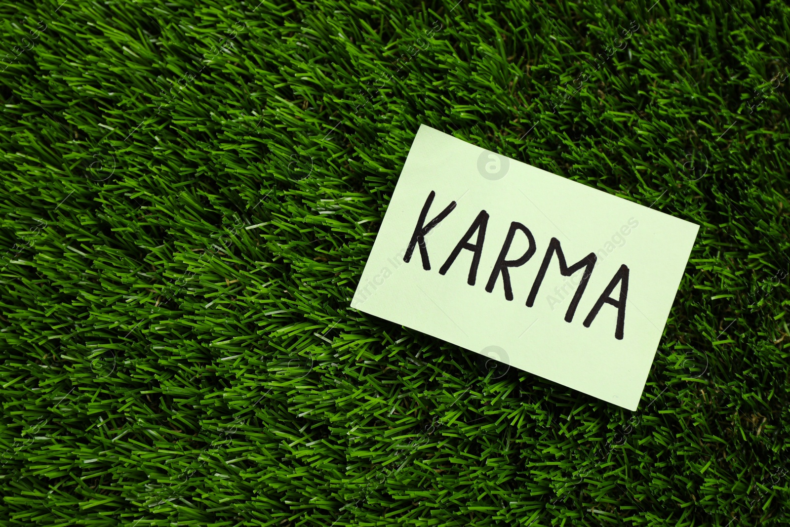 Photo of Sheet of paper with word Karma on green grass, top view. Space for text