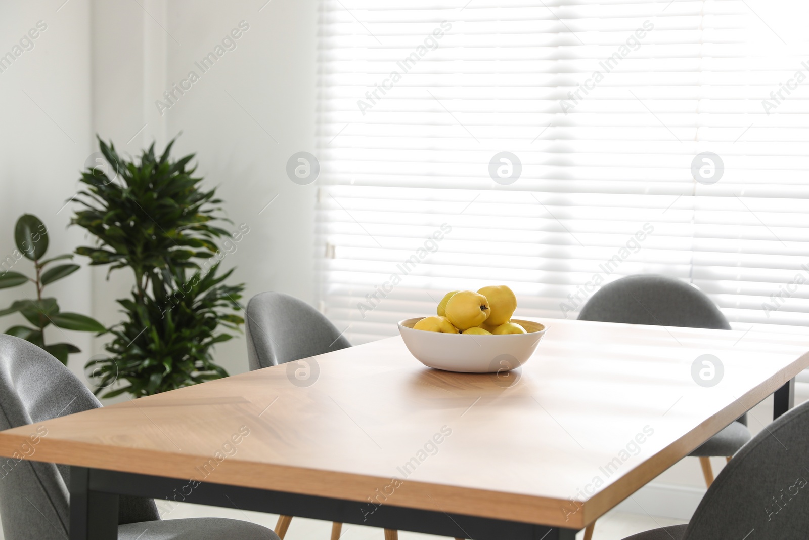 Photo of Ripe quinces on wooden table in room decorated with potted plants. Home design