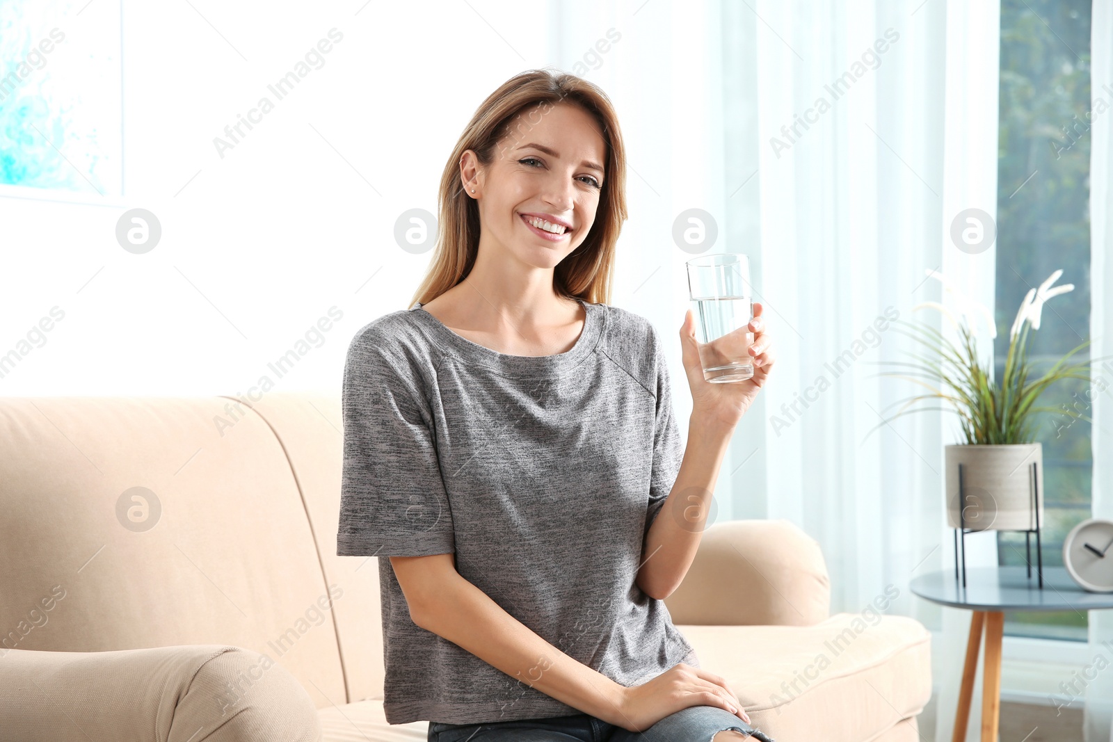 Photo of Young woman holding glass with clean water at home