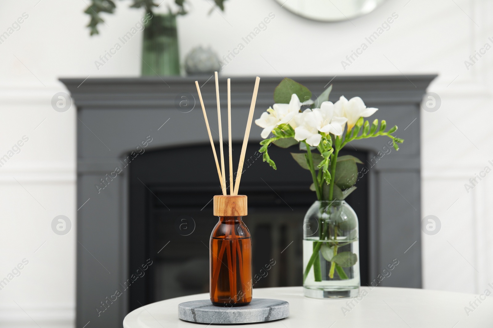 Photo of Reed diffuser and vase with bouquet on white table in room