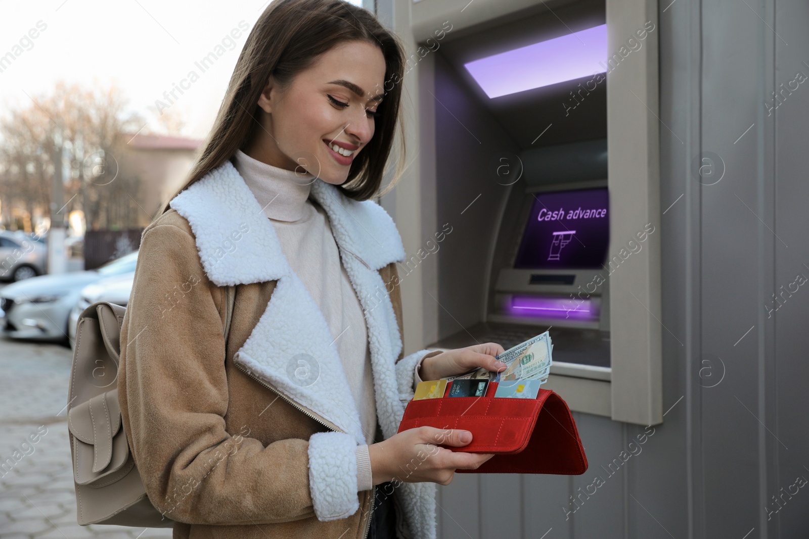 Image of Woman putting money into wallet near cash machine outdoors