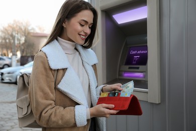 Image of Woman putting money into wallet near cash machine outdoors