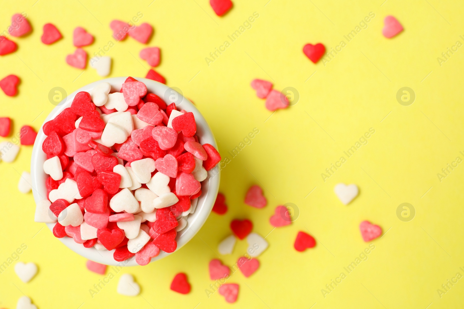 Photo of Bright heart shaped sprinkles and bowl on yellow background, flat lay. Space for text
