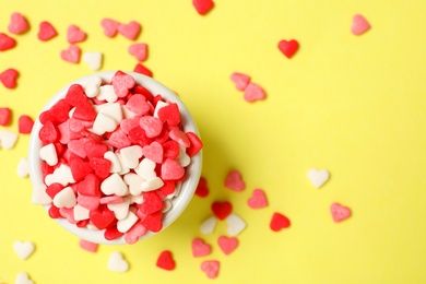 Bright heart shaped sprinkles and bowl on yellow background, flat lay. Space for text