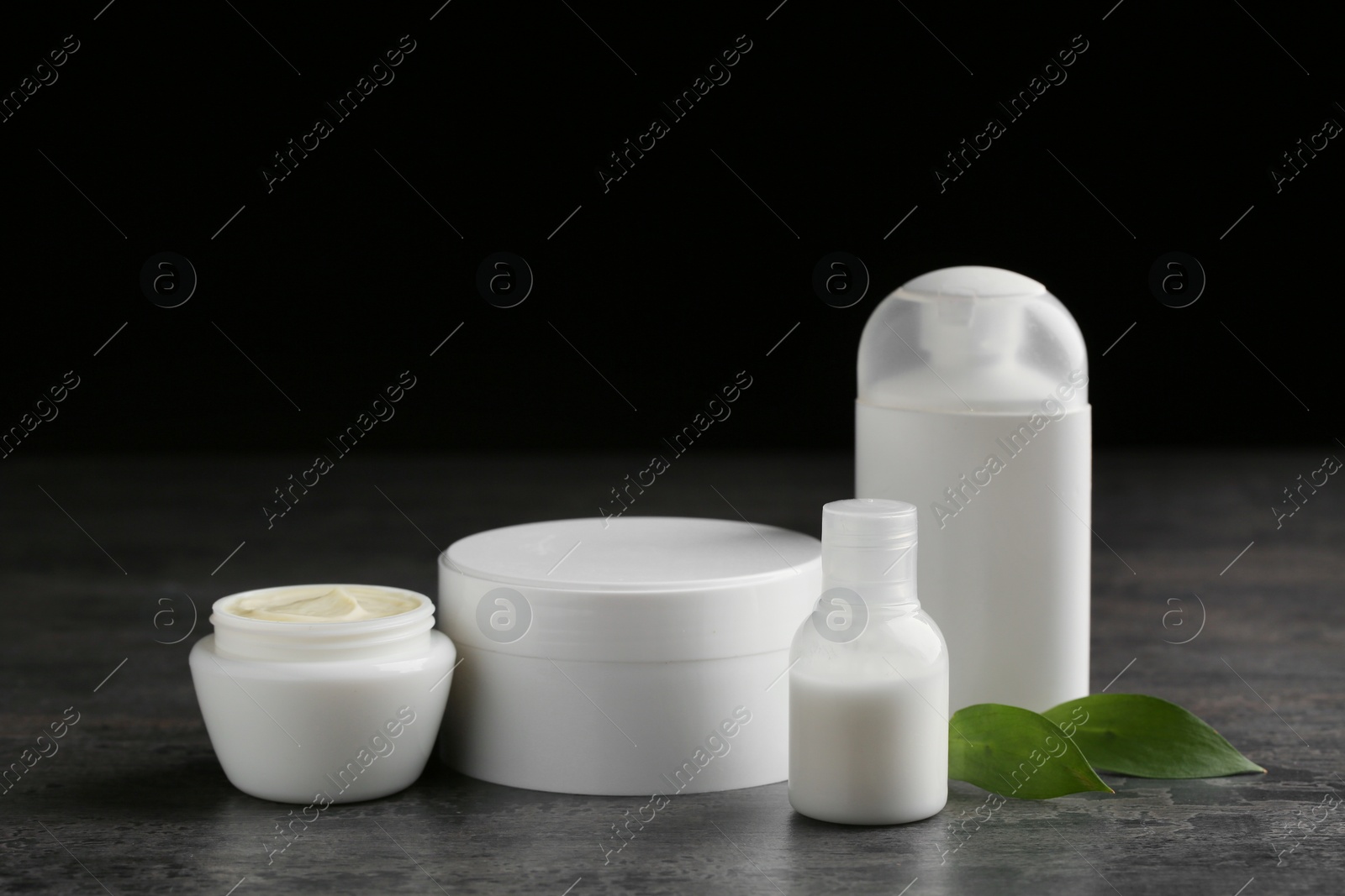 Photo of Jars with cream and bottles on dark table. Hand care cosmetics