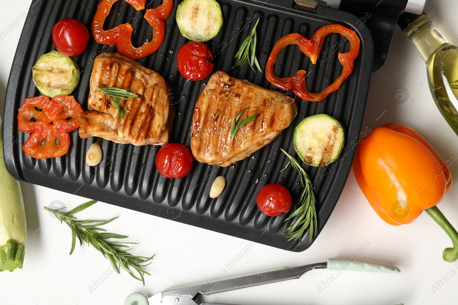 Photo of Electric grill with tasty meat, spices and vegetables on white table, flat lay